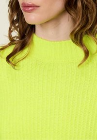 Neon żółty sweter dzianinowy o ryflowanej teksturze i wysokim dekolcie. Wykonany z miękkiego, lekkiego materiału, co podkreśla przytulny wygląd.