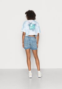 Cropped light blue tie-dye t-shirt with palm tree graphic and text, paired with light denim shorts, worn with white sneakers and socks.
