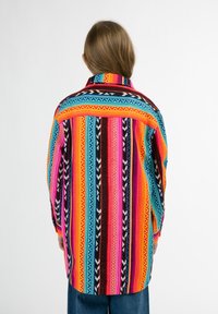 Košeľa s multikolórnym vzorom s vodorovnými pruhmi v ružovej, oranžovej, modrej a čiernej farbe. Dlhé rukávy a golier, s voľným strihom.