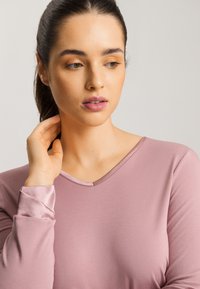 Ljusrosa långärmad topp med V-ringning. Slät textur, kontrasterande satinärmar, figurnära silhuett, minimalistisk design.