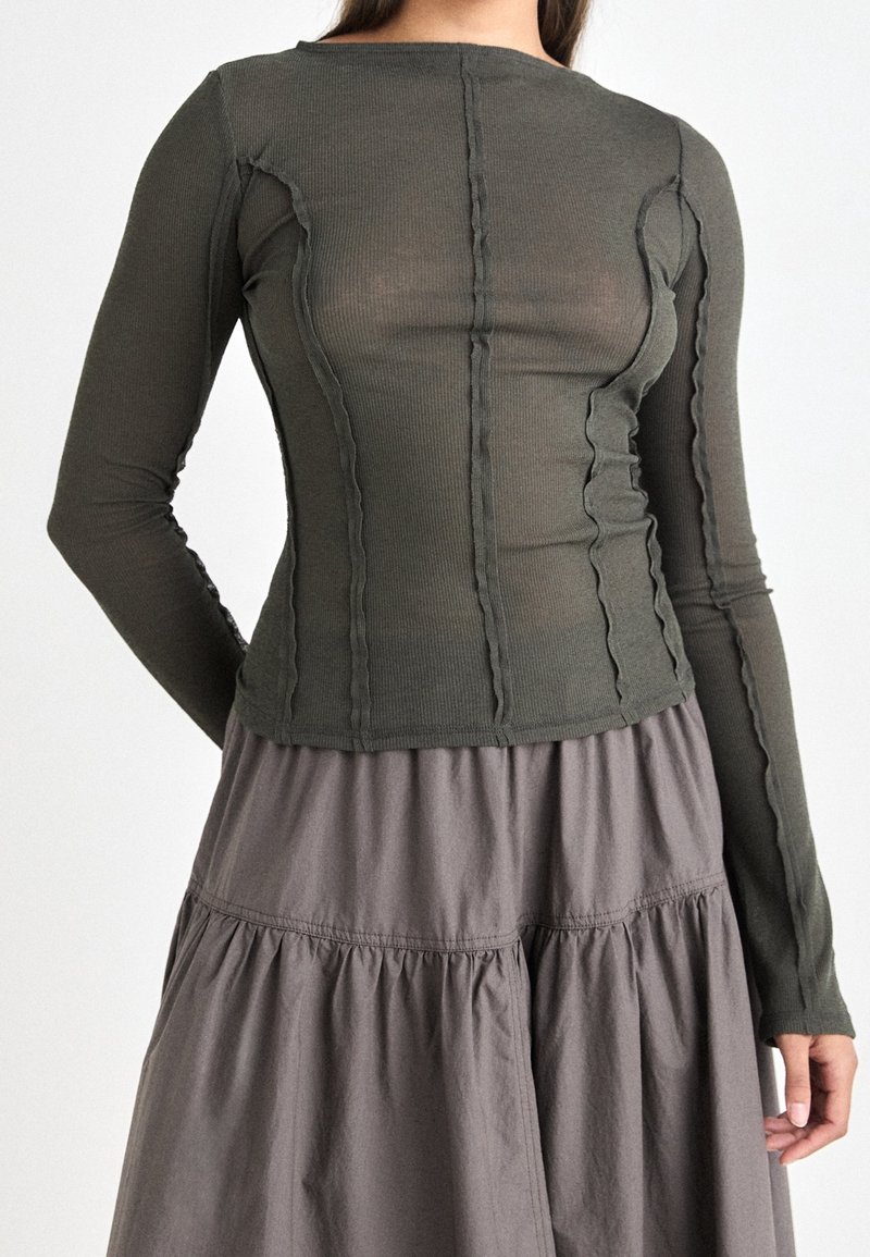Olive green long-sleeve top with ribbed texture and wavy seams, paired with a gray tiered skirt with elastic waist and soft fabric.