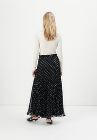 Gonna lunga nera plisettata con pois bianchi, tessuto morbido e vita elasticizzata, abbinata a un top aderente color crema a coste.