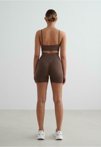 Bruin geribd sportbeha en hoogwaisted shorts set, met dunne bandjes en een textuurafwerking, gecombineerd met witte sportschoenen.