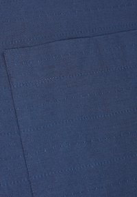 Tissu bleu marine présentant des lignes verticales et de fines coutures. Texture lisse avec un léger éclat. Comprend une petite poche plate.