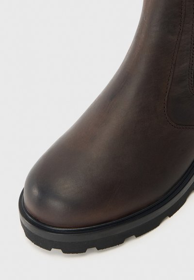 Bota de tornozelo em couro castanho com bico arredondado, parte superior texturizada e sola de borracha com padrão de sulco para tração.