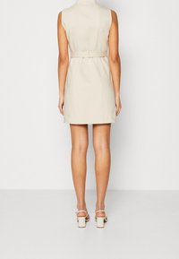 Beige sleeveless dress with a belted waist; short length; smooth fabric; paired with light cream block-heeled sandals.