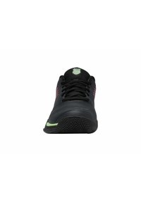 Chaussure de sport noire avec un empeigne texturée, des panneaux latéraux à motifs et une touche de vert sur la semelle. Présente une tête arrondie et un système de laçage.