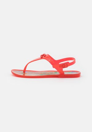 Rode platte sandalen met teenriem, verstelbare enkelsluiting en bloemmotief op de bedrukte binnenzool, zijaanzicht op witte achtergrond.
