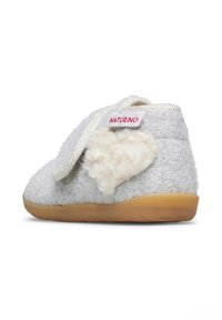 Zapatilla de casa gris con un suave acento en forma de corazón blanco y suela de goma beige. Presenta una correa de velcro y una textura brillante.