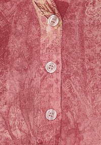 Rød stof med et diskret blomstermønster, der har tre hvide knapper med fire huller i en lodret række.