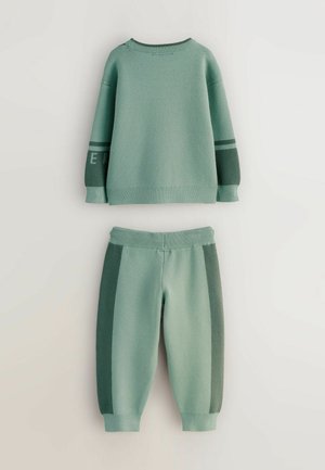 Grøn strikket sweatshirt og bukser sæt, som har rund halsudskæring, ribbede manchetter og kontrasterende sidepaneler i mørkere grønne nuancer.