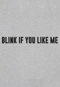 Felpa grigia con grande testo nero che recita "BATTI GLI OCCHI SE TI PIACCIO." Tessuto liscio con dettagli di design minimi.