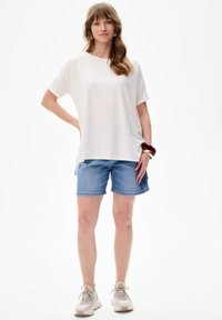 Weißes kurzärmliges Oberteil, kombiniert mit Jeansshorts. Das Oberteil hat einen lockeren Schnitt; die Shorts sind knielang und haben eine klassische blaue Waschung.