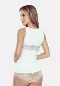 Top w kolorze jasnej kremowej z koronkowym panelem na plecach, połączony z beżową koronkową bielizną z nadrukiem kwiatowym. Gładka tekstura, dopasowany fason.