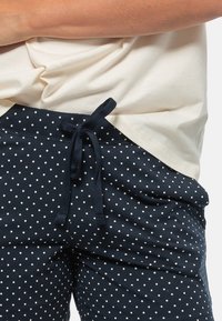 Hosen mit navyblauen Polka-Dots, einem Kordelzugbund und einem hellbeigen Oberteil, das einen lässigen Schnitt und weiches Baumwollmaterial aufweist.