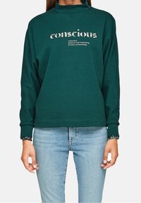 Dunkelgrüner Langarmpullover mit Stehkragen, der ein bedrucktes Textdesign und florale Akzente an den Bündchen aufweist.
