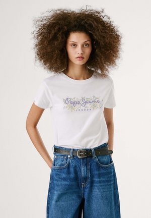 T-shirt en coton blanc présentant un design floral coloré et un texte, associé à un jean en denim bleu ample taille haute et une ceinture noire avec une boucle ronde.
