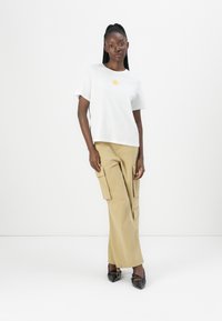 Hvit bomull t-skjorte med et gult solmotiv, kombinert med lyse beige cargo-bukser med sidelommer. Svarte spisse sko.