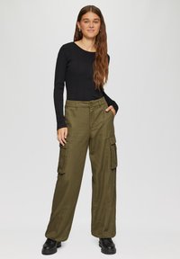 Zwart geribd longsleeve shirt gecombineerd met olijfgroene cargobroek met zijzakken, een relaxte pasvorm en zwarte veterschoenen.