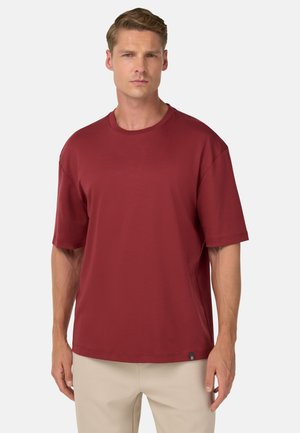 Camiseta roja de manga corta hecha de material suave, con cuello redondo y un corte relajado, que presenta una pequeña etiqueta con el logo en el dobladillo.