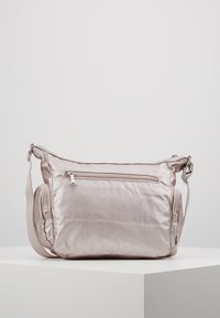 Jasnoróżowa satynowa torba na ramię z regulowanym paskiem, przednią kieszenią na zamek oraz dwoma bocznymi komorami na zamek, umieszczona na białym piedestale.