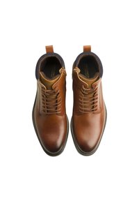 Des bottes en cuir marron présentent une finition lisse, un laçage à l'avant et un col contrastant en marine. Talon renforcé et tirant pour faciliter l'enfilage.