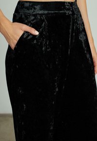 Zwarte fluwelen broek met een gladde textuur, wijd uitlopende pijpen, zijzak en een verborgen rits in de taille voor sluiting.