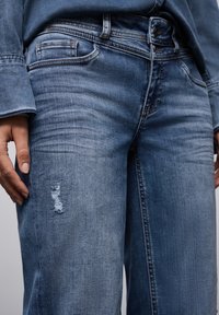 Jeans de mezclilla de color azul claro con un corte relajado, que presentan un desgastado en el muslo y un diseño estándar de cinco bolsillos.