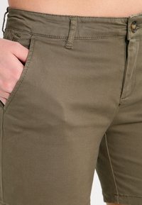Pantaloni corti verde oliva realizzati in morbido misto cotone, con tasche laterali, chiusura con bottone e dettagli di cucitura classici.