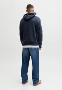 Laivastonsininen huppari, jossa kiristysnauhallinen huppu, puuvillasekoitemateriaalia. Yhdistetty väljästi istuviin sinisiin farkkuihin ja beigeihin jalkineisiin.