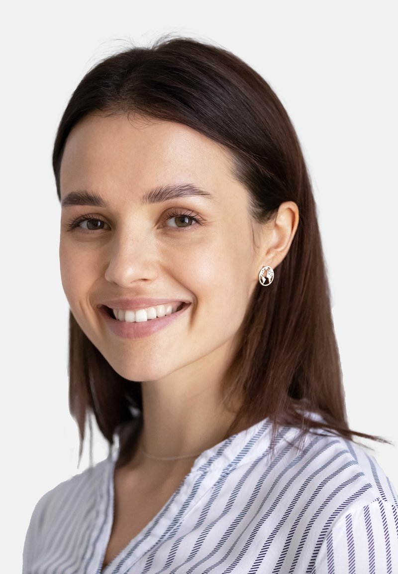 Ett par runda silverörhängen med ett träddesign, bärs av en kvinna med mörkbrunt hår, klädd i en randig vit och blå skjorta.