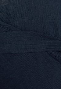 Tecido texturizado em azul marinho escuro com um design ribeteado e um detalhe de faixa cruzada, proporcionando uma aparência em camadas.