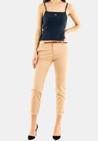 Débardeur marine, pantalon beige court avec des ourlets roulés, ceinture en cuir marron et talons noirs. Logo discret sur le débardeur. Texture de tissu lisse.
