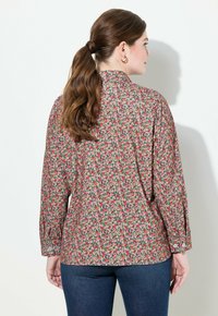 Blusa floreale con sfondo rosa, caratterizzata da piccoli fiori multicolori, polsini con bottone e colletto a punta. Design morbido e comodo.