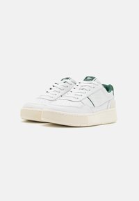 White sneakers with green accents, leather upper, textured rubber sole, round toe, and six eyelets for laces. Embossed logo on the side.