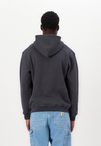 Dunkelgrauer Kapuzenpullover aus Baumwollmischung, mit einer großen Kapuze und gerippten Bündchen. Getragen mit hellblauen Cargo-Hosen.