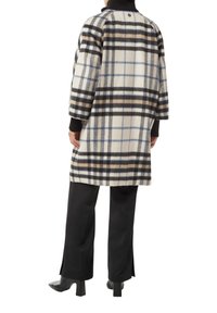 Karierten Mantel in Creme, Schwarz, Blau und Braun; hat eine lockere Passform, abgesenkte Schultern und gerippte schwarze Bündchen. Kombiniert mit schwarzen Hosen und High Heels.