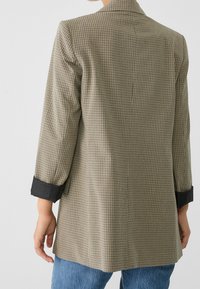 Rutig kavaj i beige och svart, med en skräddarsydd passform och svarta manschetter. Materialet har en mjuk yta med en strukturerad design.