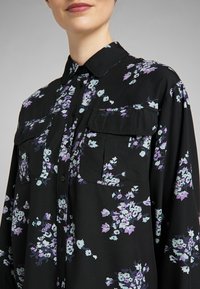Svart blommig skjorta med lila och ljusblå mönster, med knappstängning fram, två bröstfickor och klassisk krage.