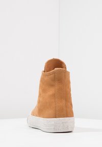 Tan leather ankle boot with a textured upper, slightly padded collar, and a white speckled rubber sole. Back view highlights stitching details.