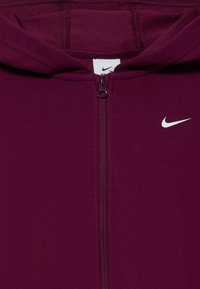 Fioletowa bluza z kapturem na zamek, wykonana z miękkiego materiału. Posiada zamek z przodu, kaptur oraz małe białe logo Nike po lewej stronie.