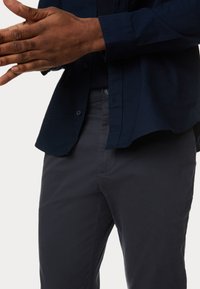 Camicia button-up blu scuro con una texture morbida, abbinata a pantaloni antracite con una finitura liscia e dettagli sottili sulle tasche.