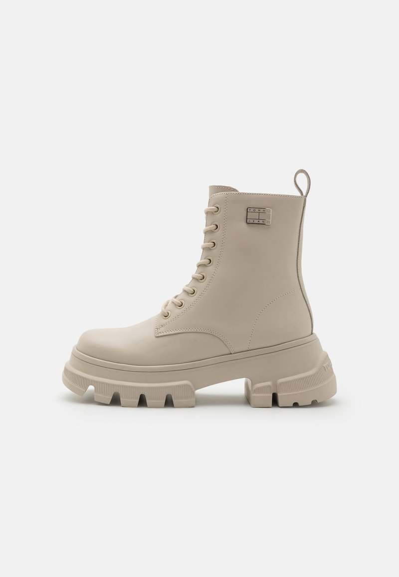 Botte de combat beige à lacets avec semelle épaisse crantée et languette arrière, vue de profil sur fond uni.
