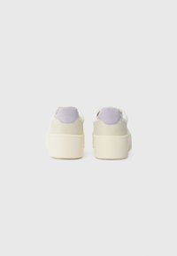 Sneakers with a low top, featuring a cream base, light purple suede accents on the heel, and a textured rubber sole.