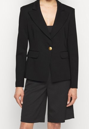 Blazer nero con un solo bottone dorato, design su misura, due tasche frontali, tessuto liscio, revers a punta, abbinato a pantaloni corti neri.