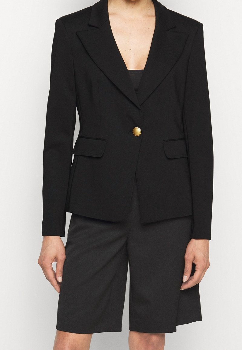 Černý blazer s jedním zlatým knoflíkem, dobře střižený design, dvě přední kapsy, hladká tkanina, klopové límce, kombinovaný s černými šortkami.
