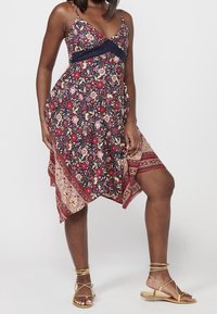 Robe à imprimé floral avec un corsage bleu marine, des bretelles spaghetti réglables, un ourlet asymétrique et une bordure à motifs avec des accents rouges et dorés.