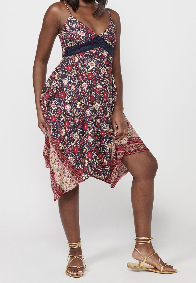 Robe à imprimé floral avec un corsage bleu marine, des bretelles spaghetti réglables, un ourlet asymétrique et une bordure à motifs avec des accents rouges et dorés.