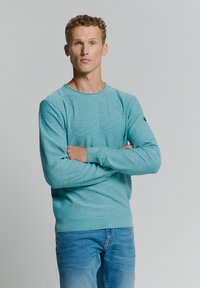 Lichtblauwe ronde hals trui met lange mouwen en gestructureerde stof. Gekozen in combinatie met denim jeans, wat een casual look toont.