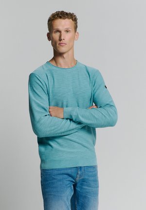 Lichtblauwe ronde hals trui met lange mouwen en gestructureerde stof. Gekozen in combinatie met denim jeans, wat een casual look toont.